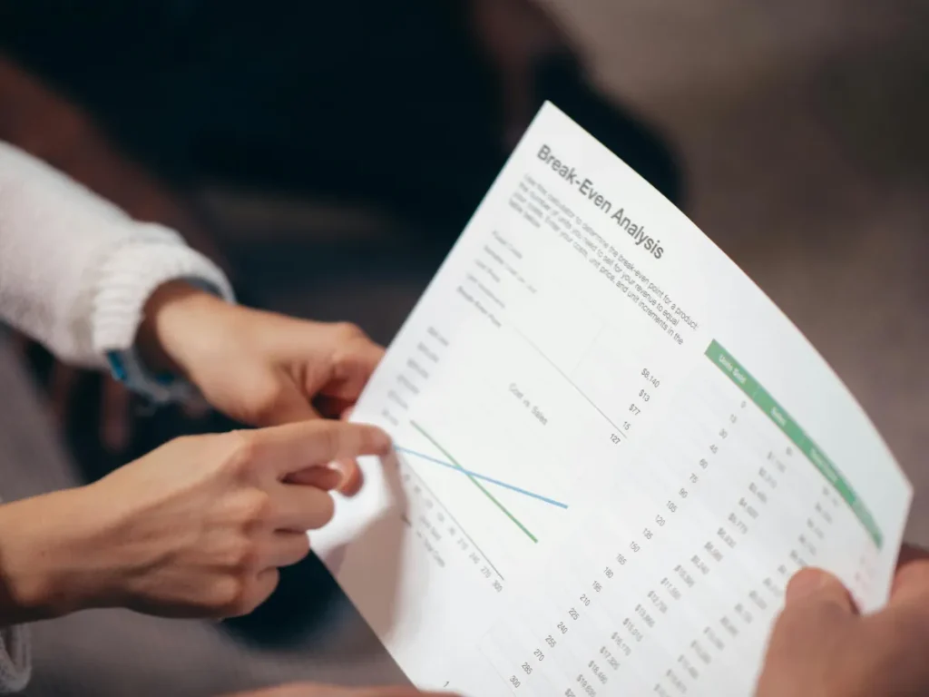 Tangan sedang mendiskusikan dokumen analisis break even point dalam rapat bisnis